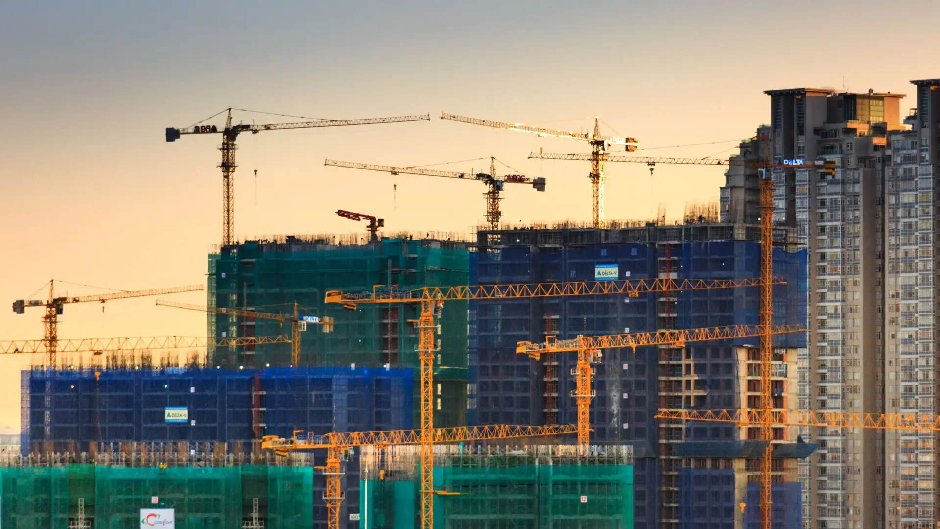Edificios en construcción con grúas, andamios y redes de seguridad al atardecer